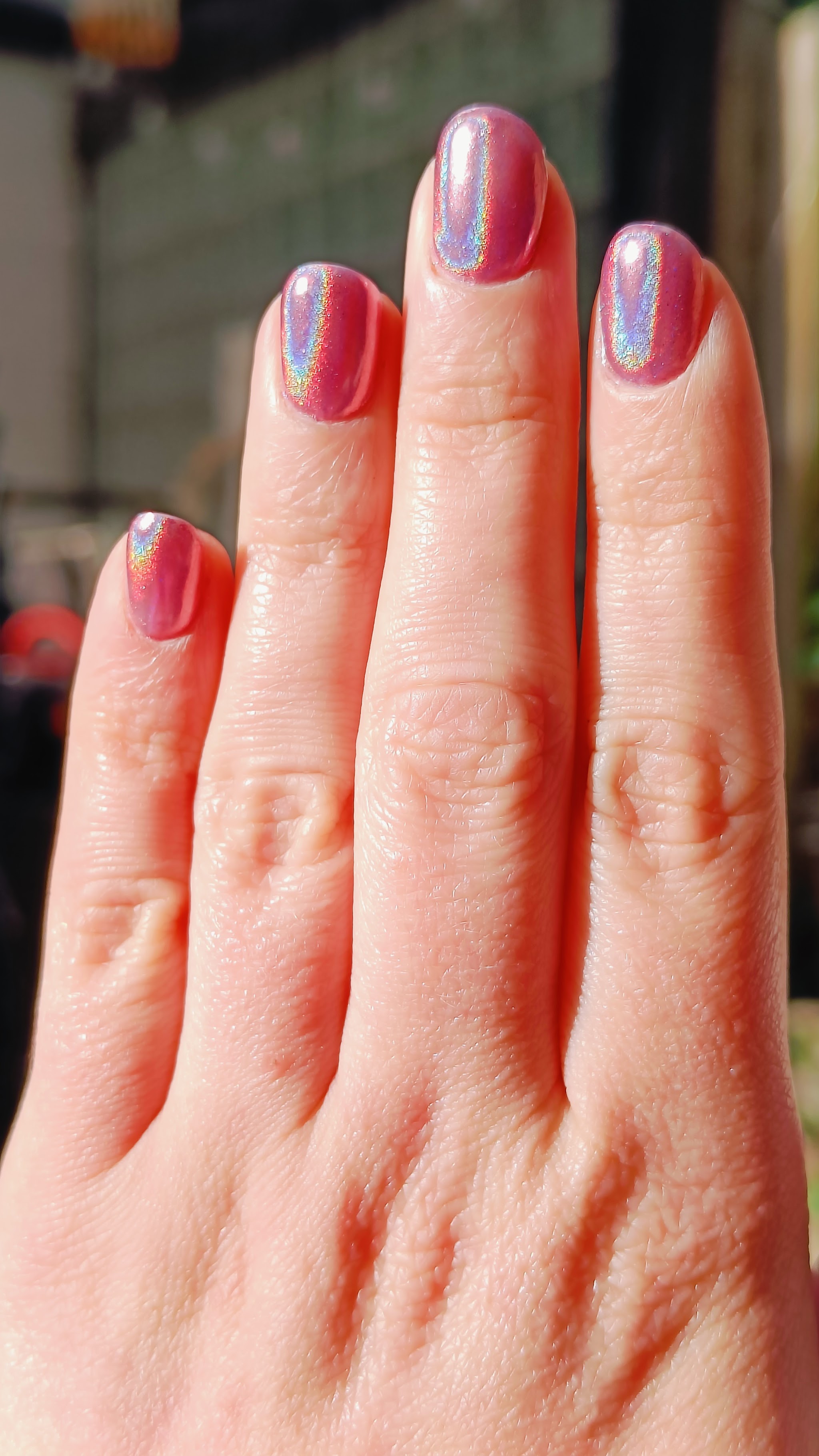 Hand met nagels in roze chrome, in het zonlicht