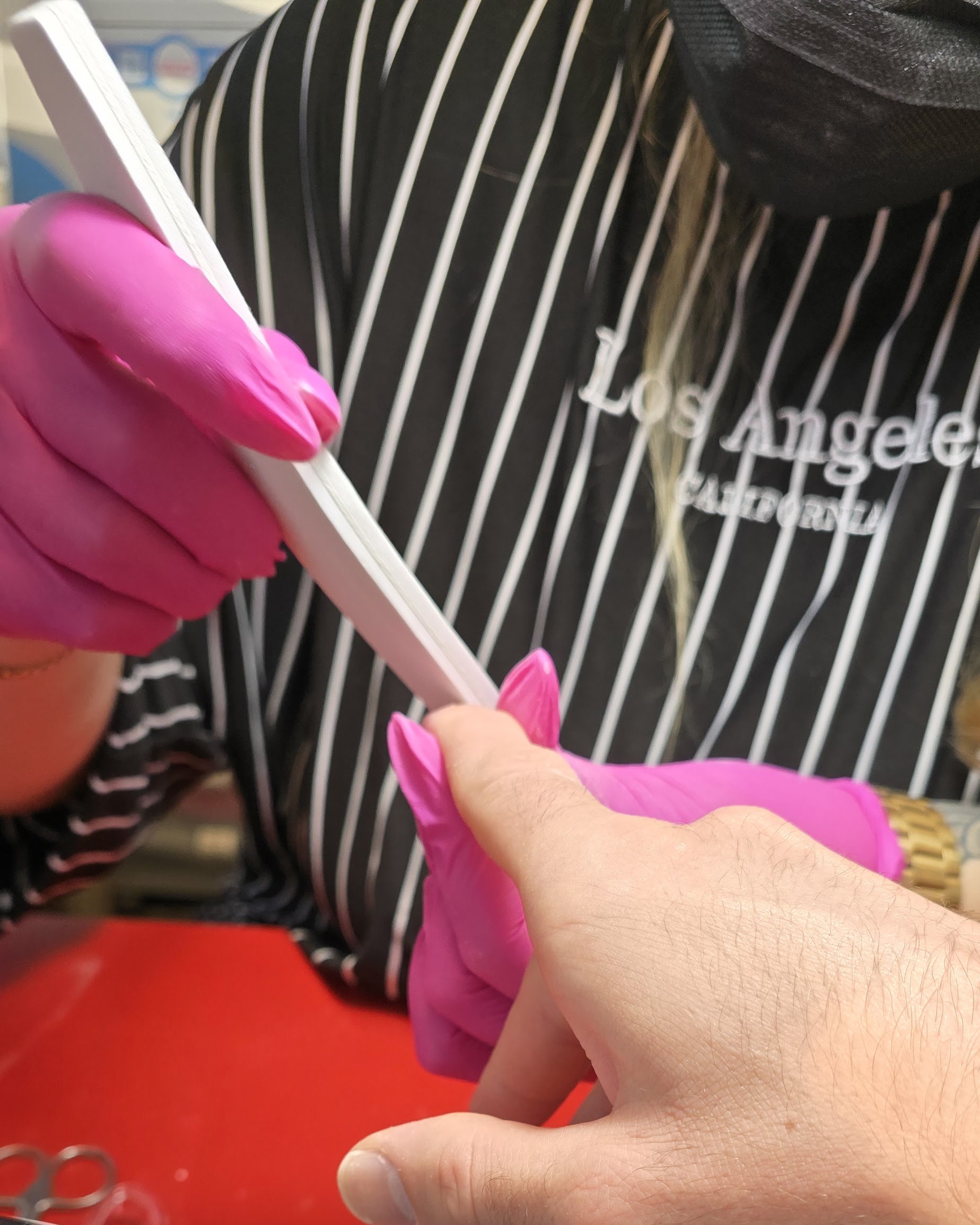 Valeriia vijlt met roze handschoenen de nagels van een klant
